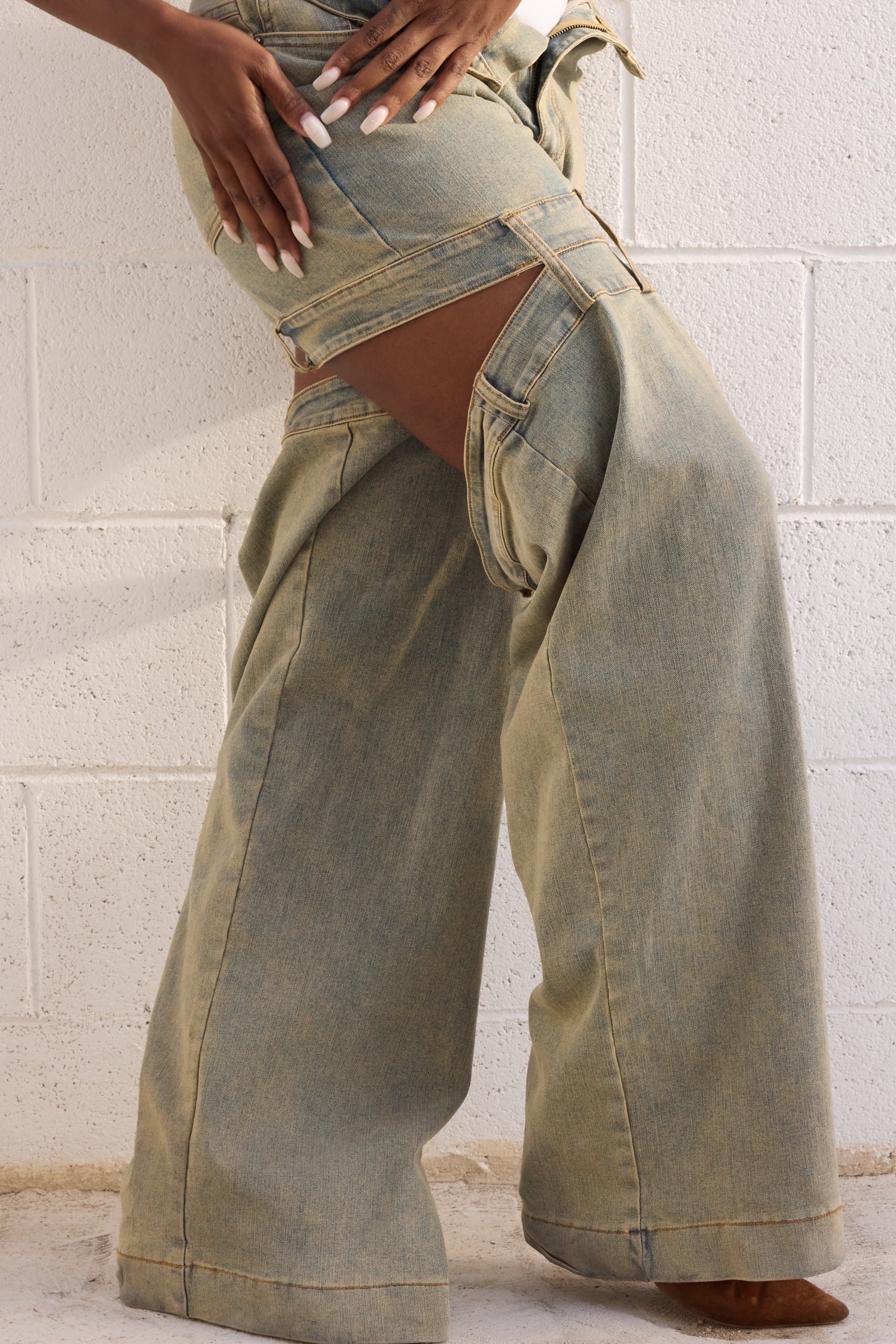 Person wearing light green wide-leg jeans against a white brick wall.