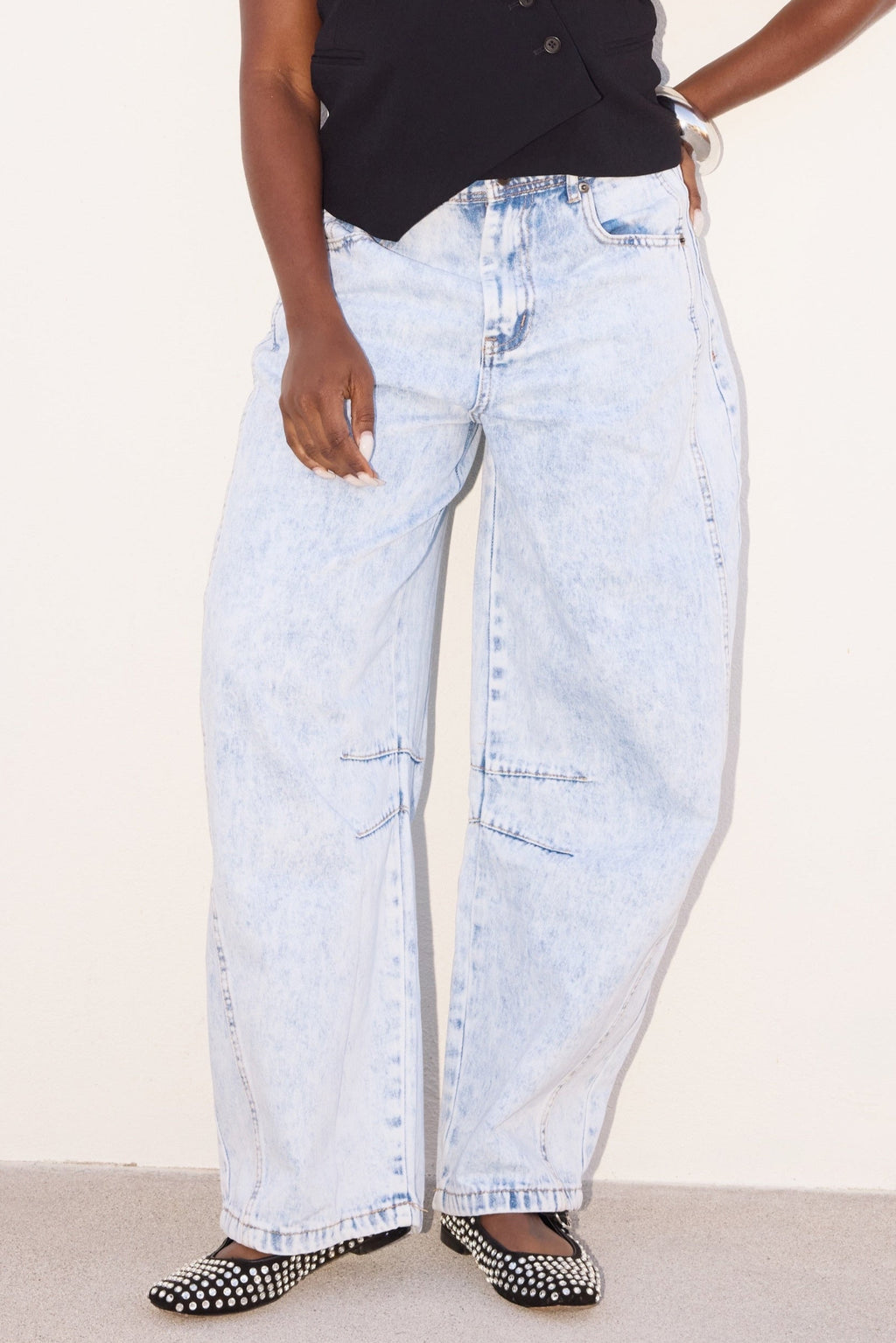 Woman wearing a black sleeveless top and light blue jeans against a white background