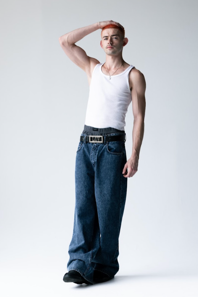 Person wearing a white tank top and blue jeans on a plain background