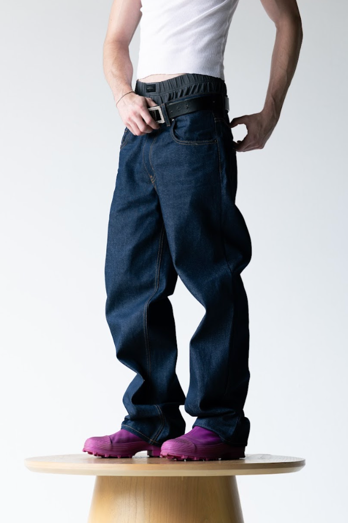 Person wearing dark blue pants and purple shoes standing on a wooden stool against a white background