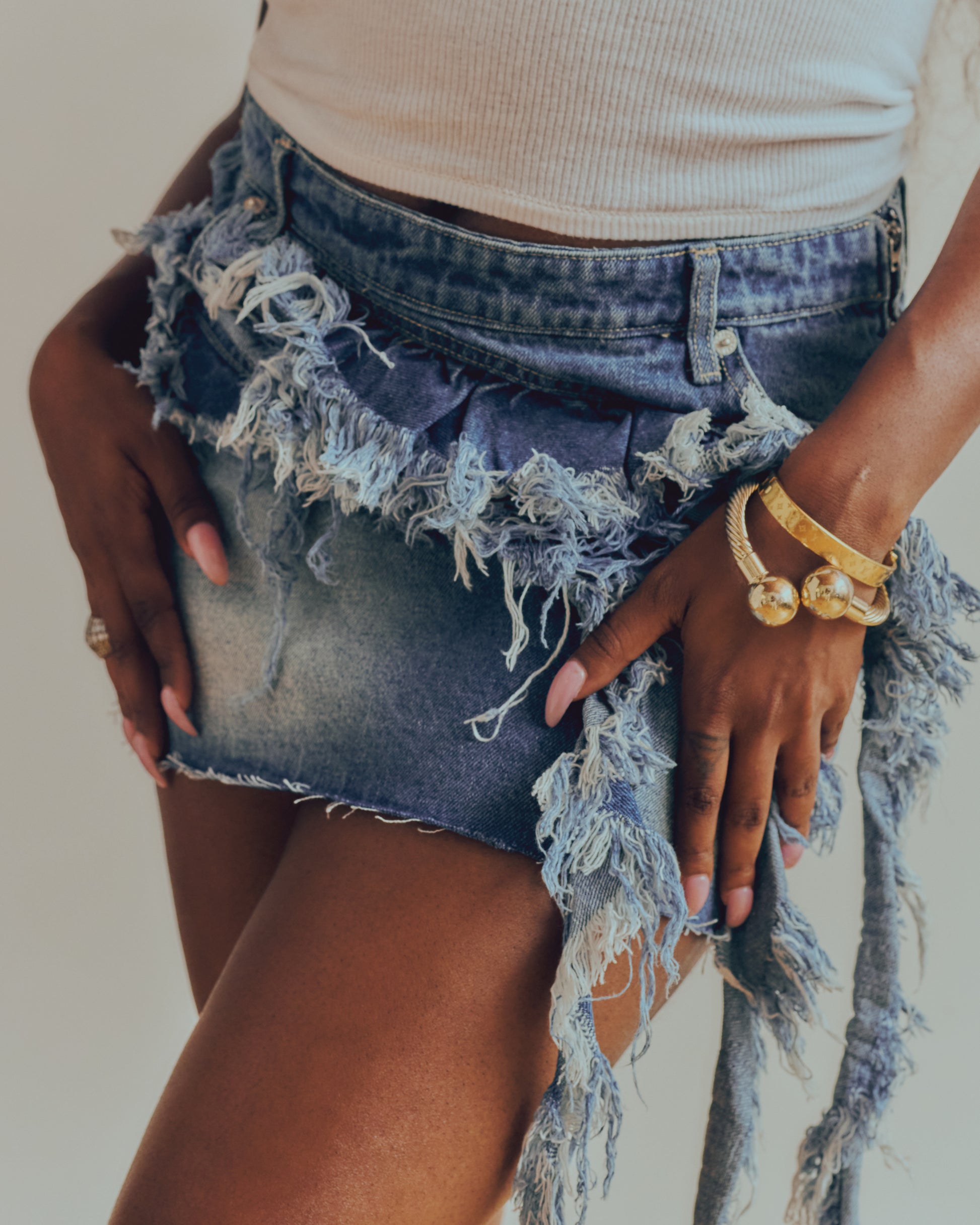 Person wearing a distressed denim skirt with a neutral background