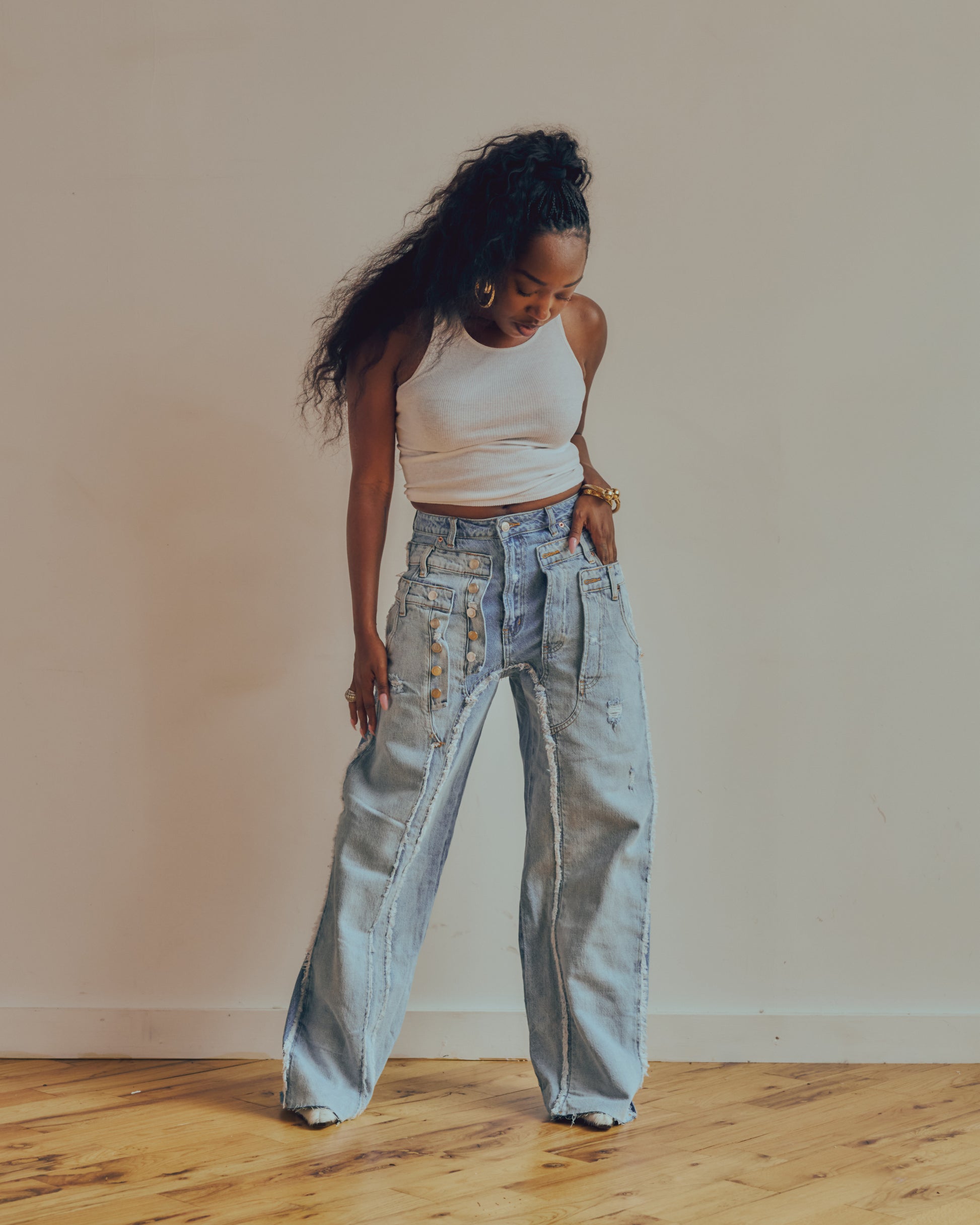 Woman wearing light blue jeans and a white top against a plain wall.