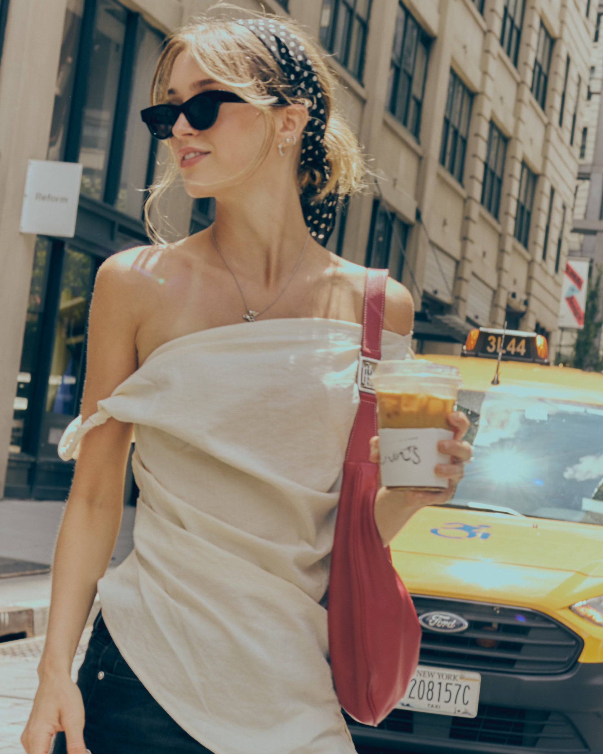 Woman in a city street holding a drink, with a yellow taxi in the background