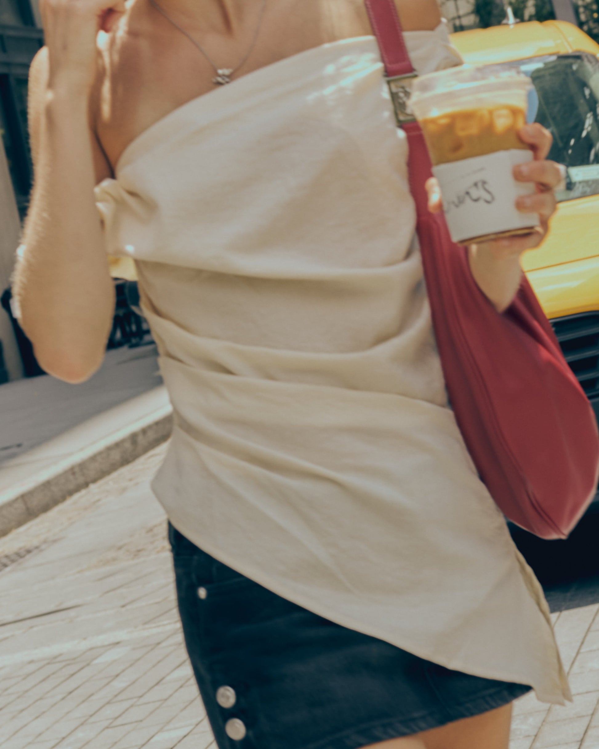Woman walking on a city street holding a drink, wearing a white top and black skirt.