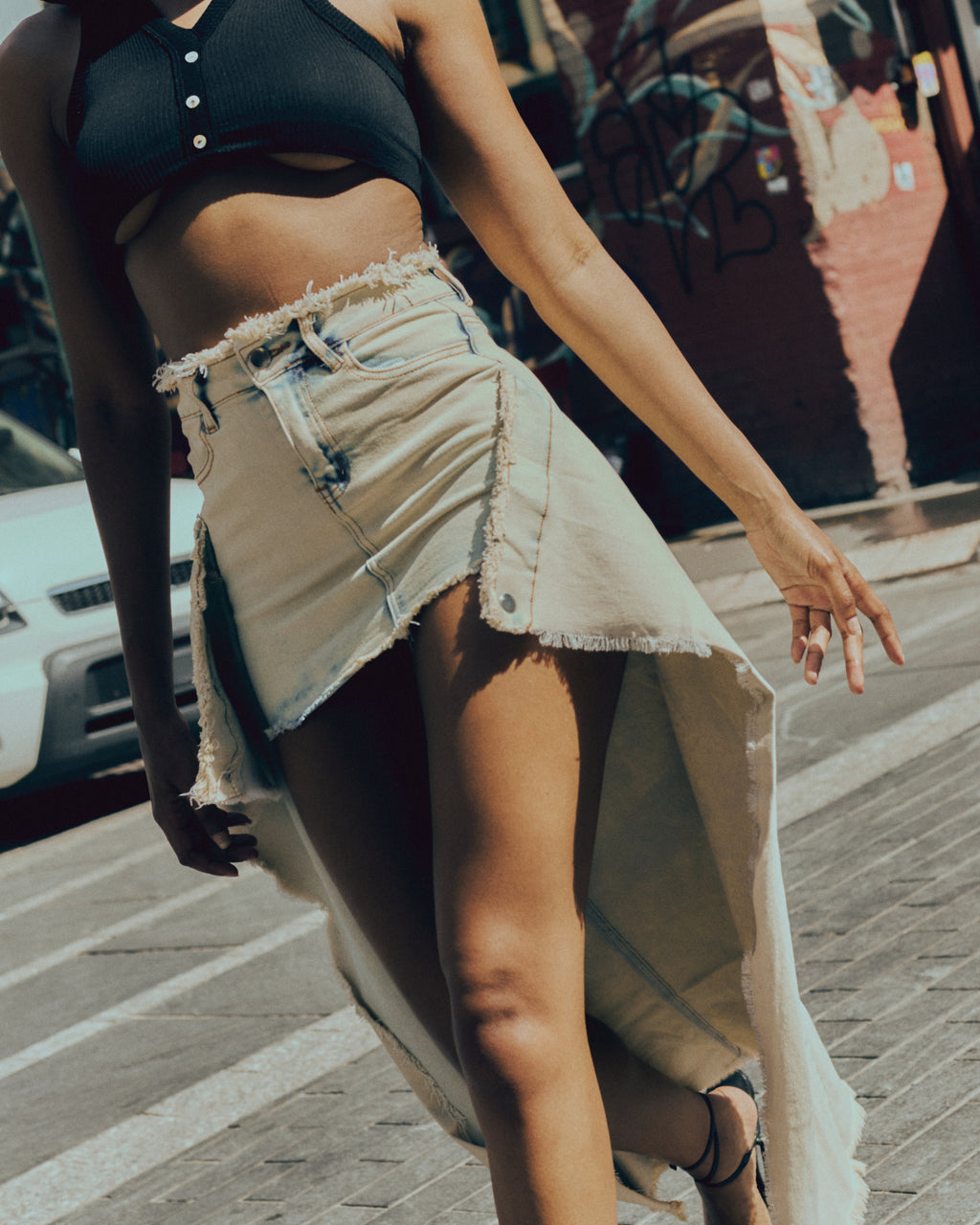 Person wearing a black crop top and beige denim skirt on a street.