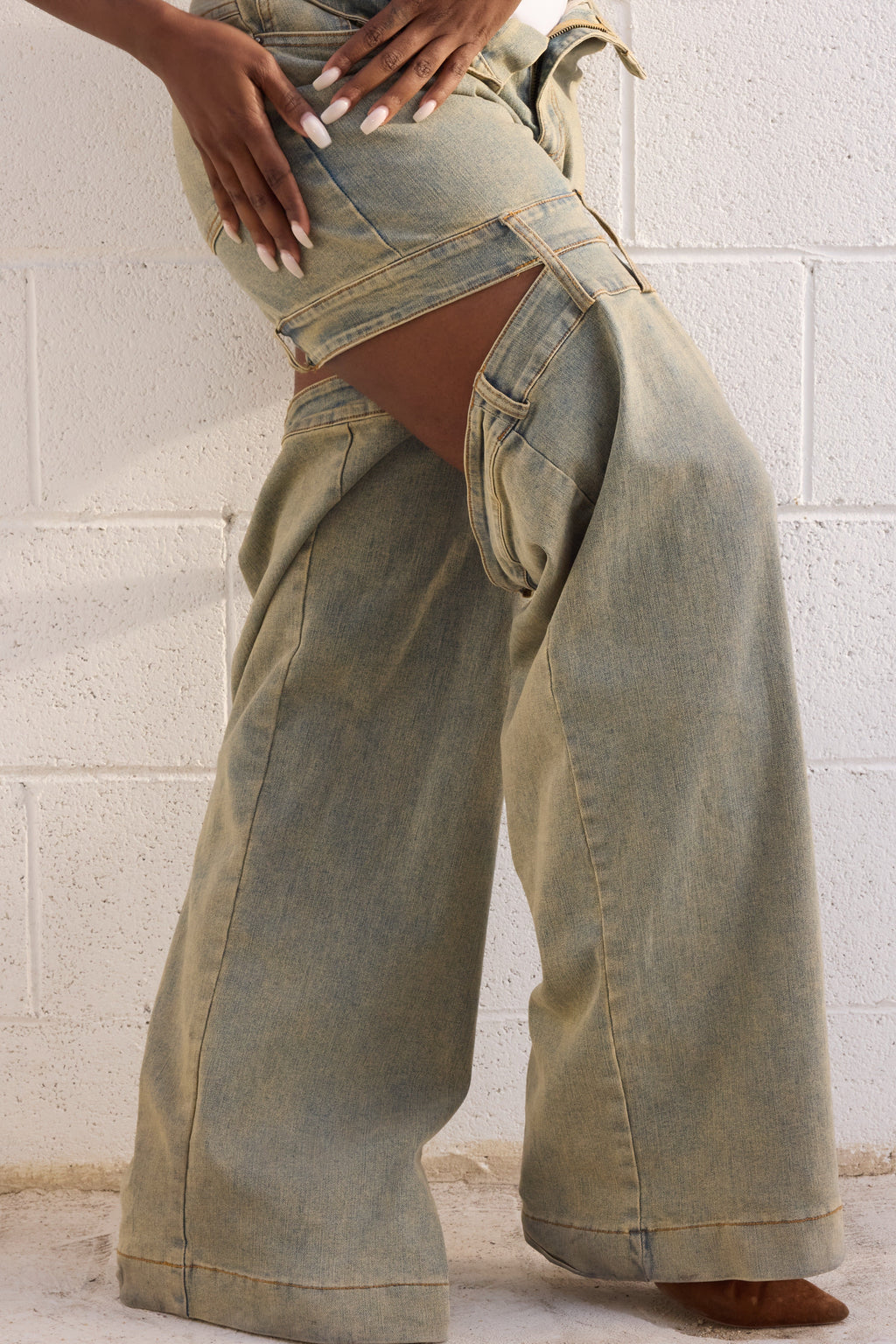 Person wearing light green wide-leg jeans against a white brick wall.