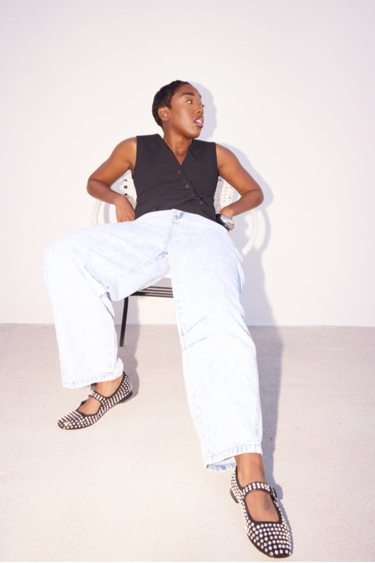 Person sitting on a chair wearing a black sleeveless top, white pants, and patterned shoes.